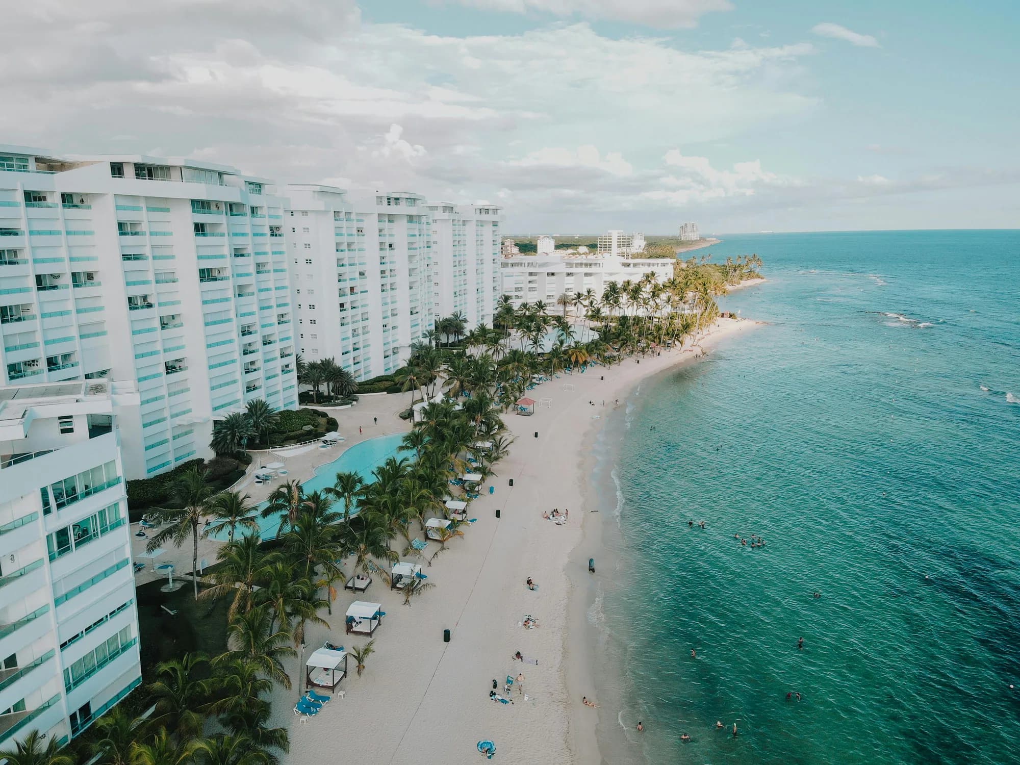 Vista aérea de condominios frente a una playa de arena blanca y agua turquesa