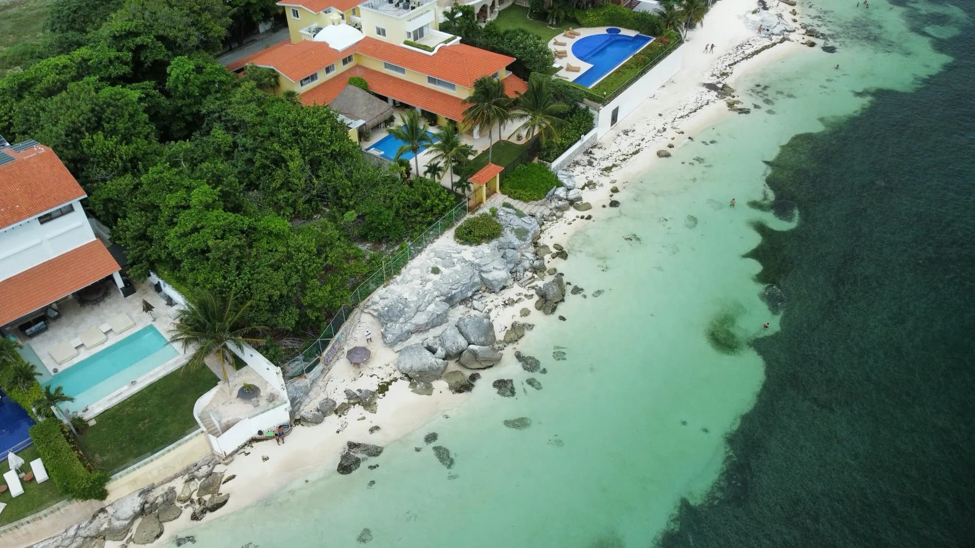 Vista aérea de casas frente al mar con techos de teja y piscinas, junto a la orilla rocosa